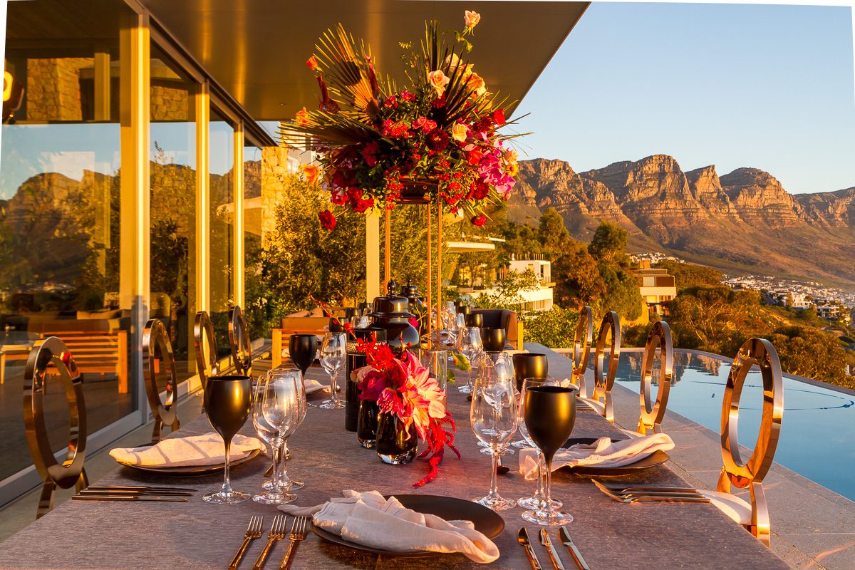Dining table on balcony of a villa overlooking a swimming pool and mountains in the background