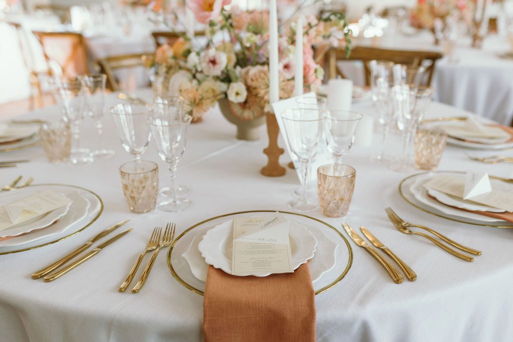 Wedding reception table with white table cloth and terracotta coloured napkins and gold cutlery